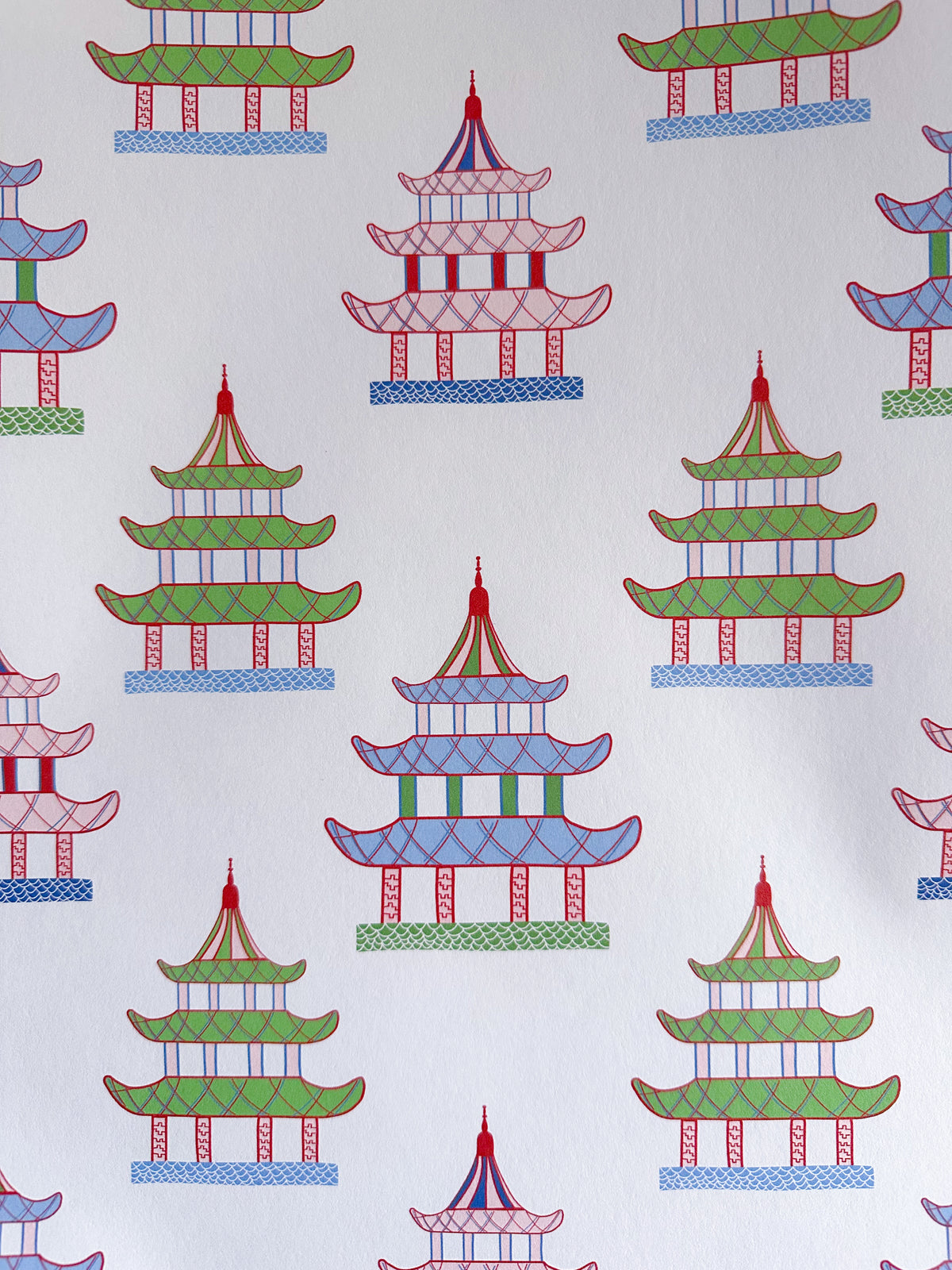 Closeup of Little Temples white wallpaper featuring a repeating pattern of pagoda buildings in green, pink, blue
